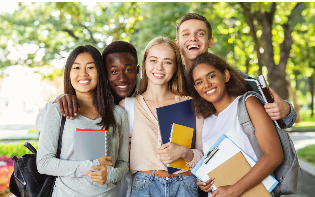 Group of 5 diverse international students pose for a photo holding their backpacks and notebooks.