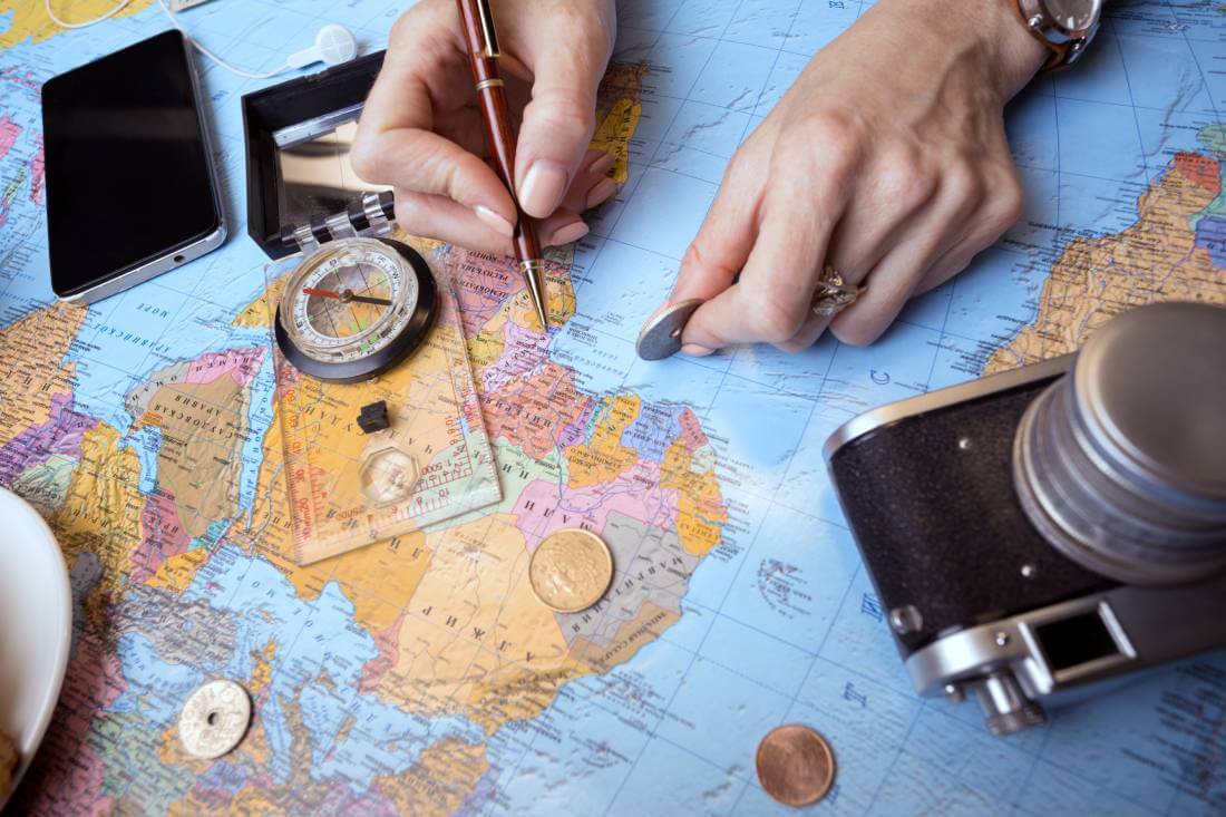 A persons using a map, compass, and pen to plan a trip around the world.