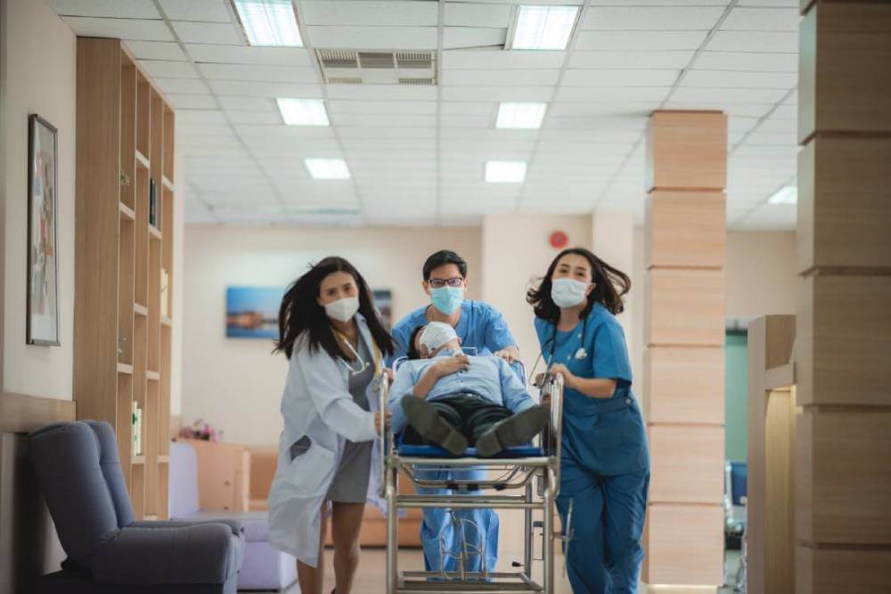 3 doctors run with a patient on a stretcher in an emergency room.
