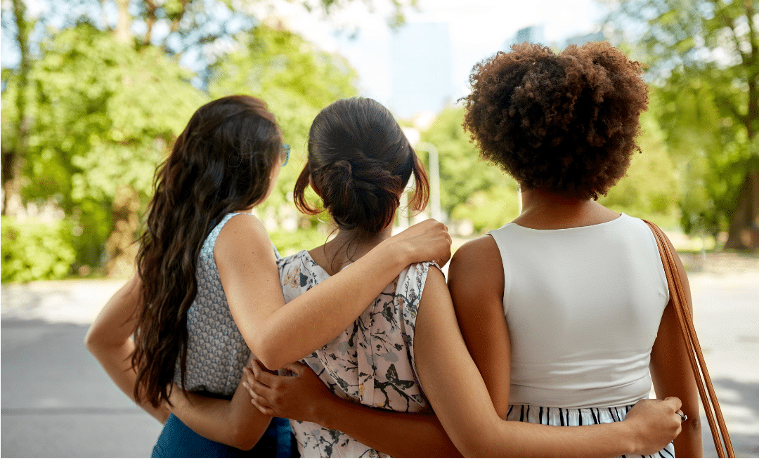 Three women of different ethnicities wrap their arms around each other